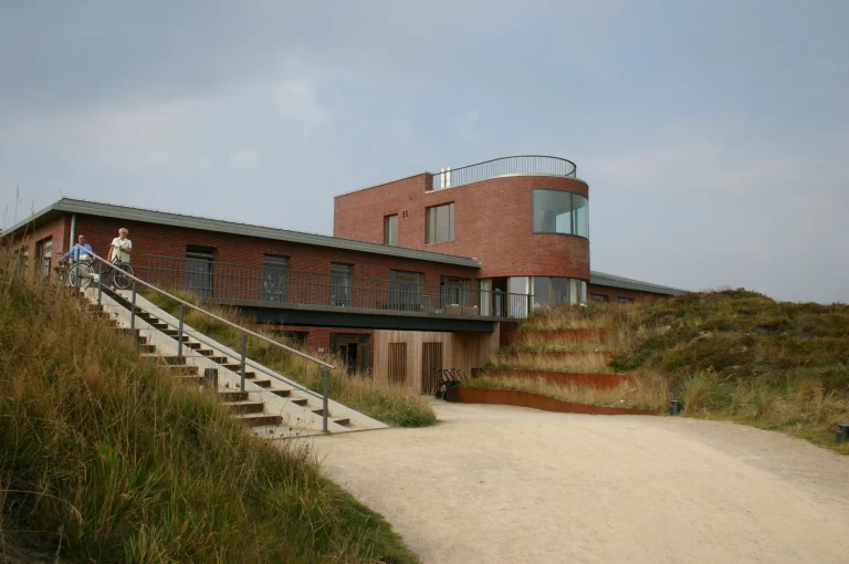 Golfhaus Budersand auf Sylt mit roter Ziegelfassade und rundem Baukörper, eingebettet in die Dünenlandschaft